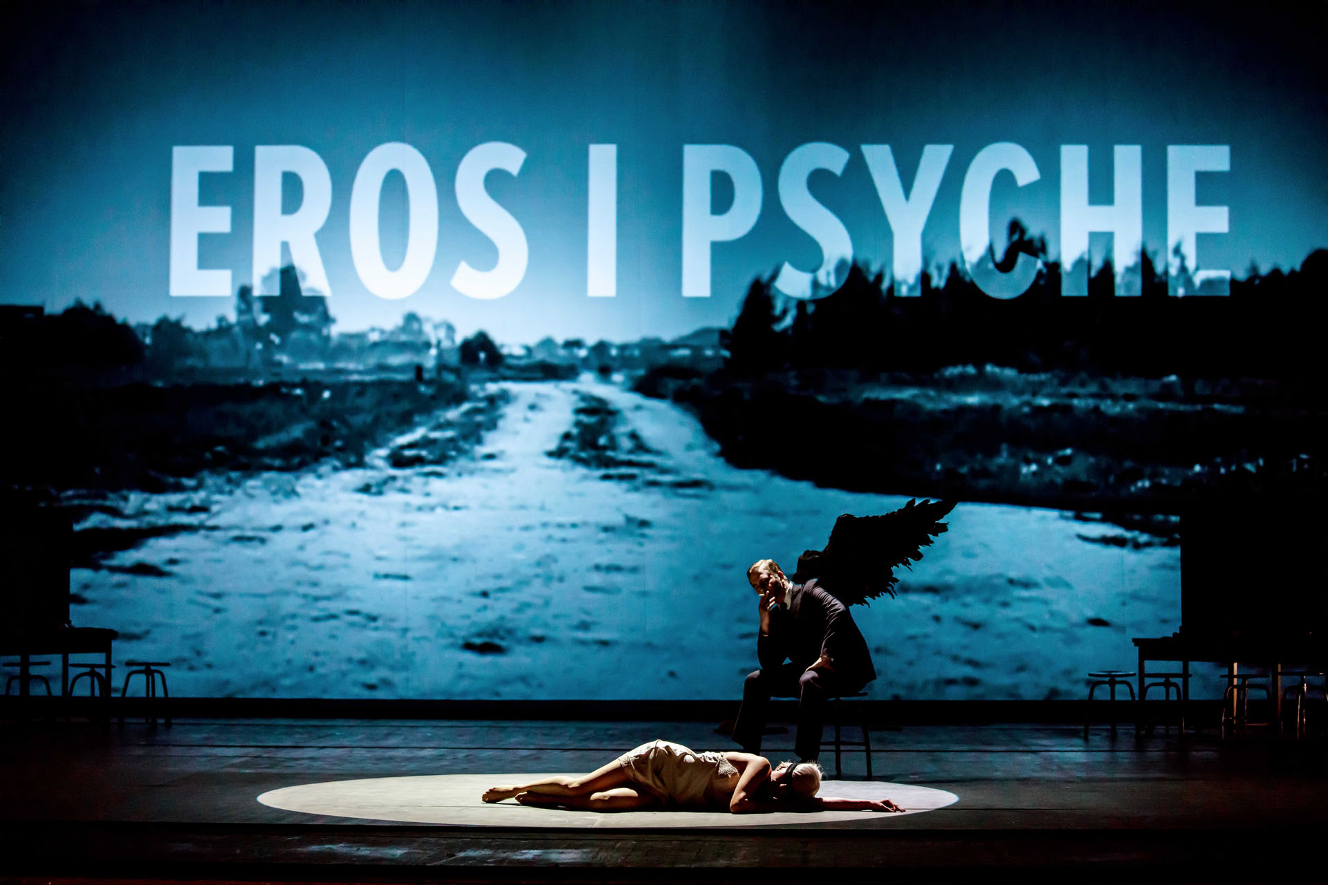 Na zdjęciu Eros leżąca na scenie i siedzący na stołku Eros ze skrzydłami. W tle napis Eros i Psyche.