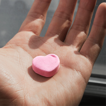 Różowa pigułka w kształcie serca na dłoni