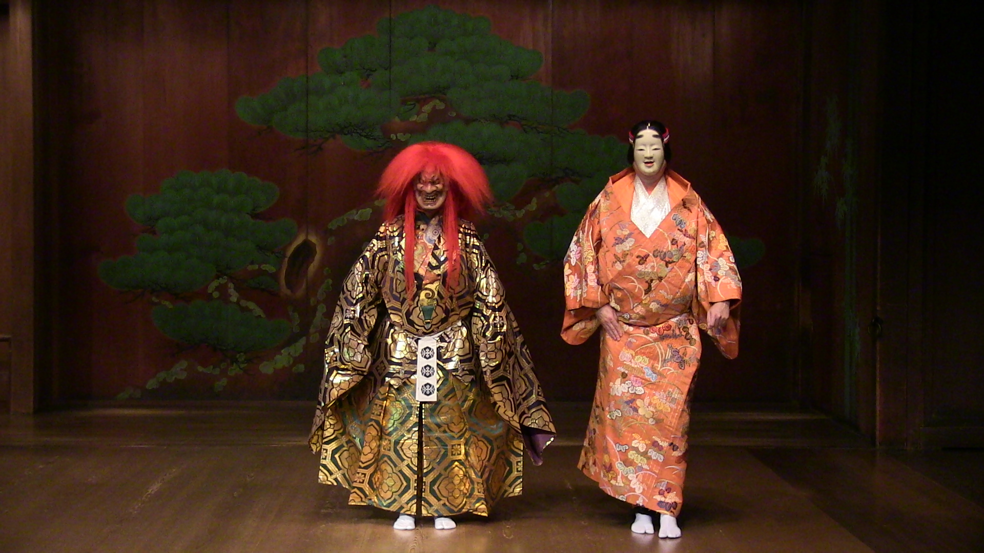 A scene from a play: In the centre of the stage two actors wearing colorful kimonos and Japanese masks