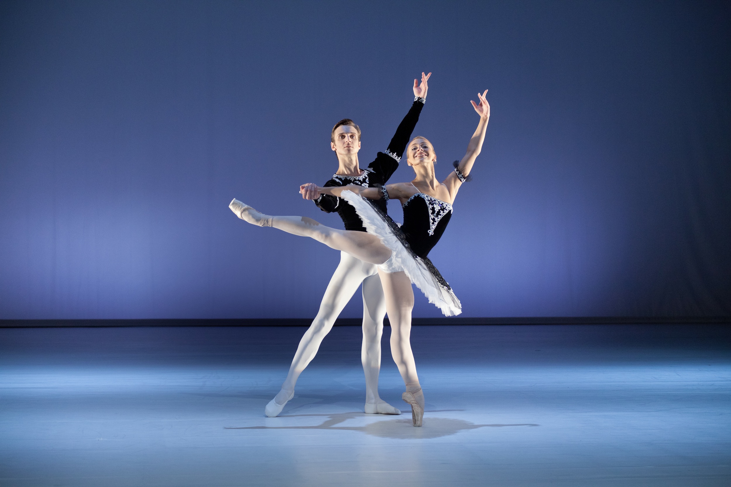 para tancerzy baletowych w pozycji stojącej, z lewą ręką uniesioną do góry, tancerka stoi na palcach lewej nogi, przytrzymywana za rękę przez tancerza