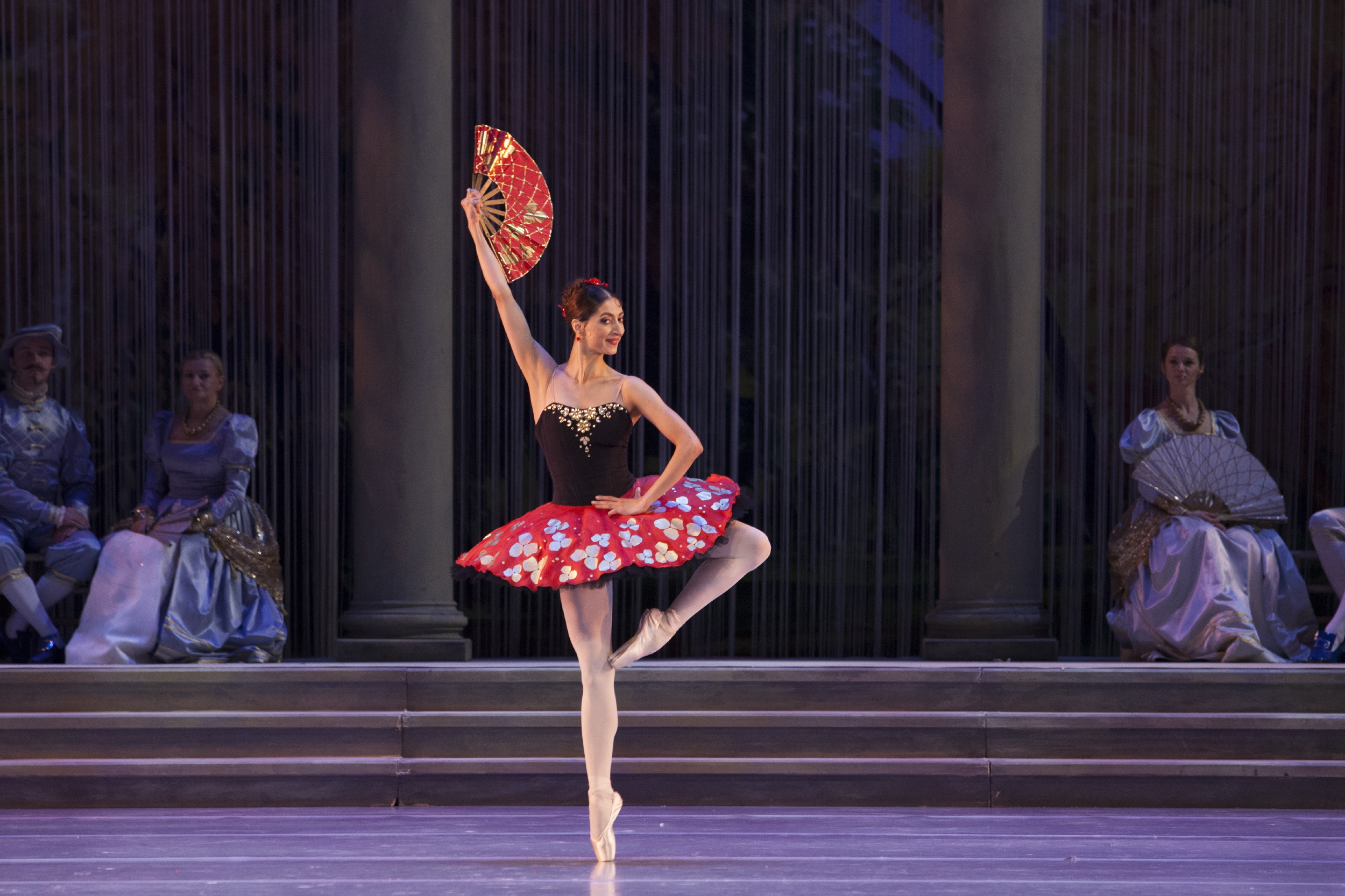 Pictured: Soloist Chinara Alizade onstage in a Spanish costume holding a fan in her raised arm.