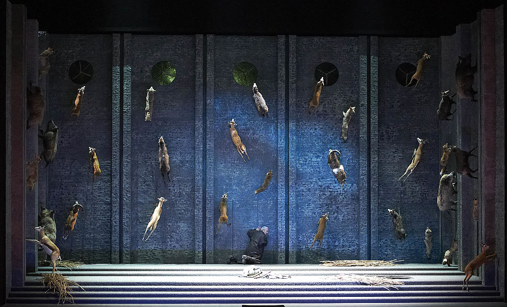 Na zdjęciu scenografia ze zwierzętami, śpiewak klęczy na środku sceny