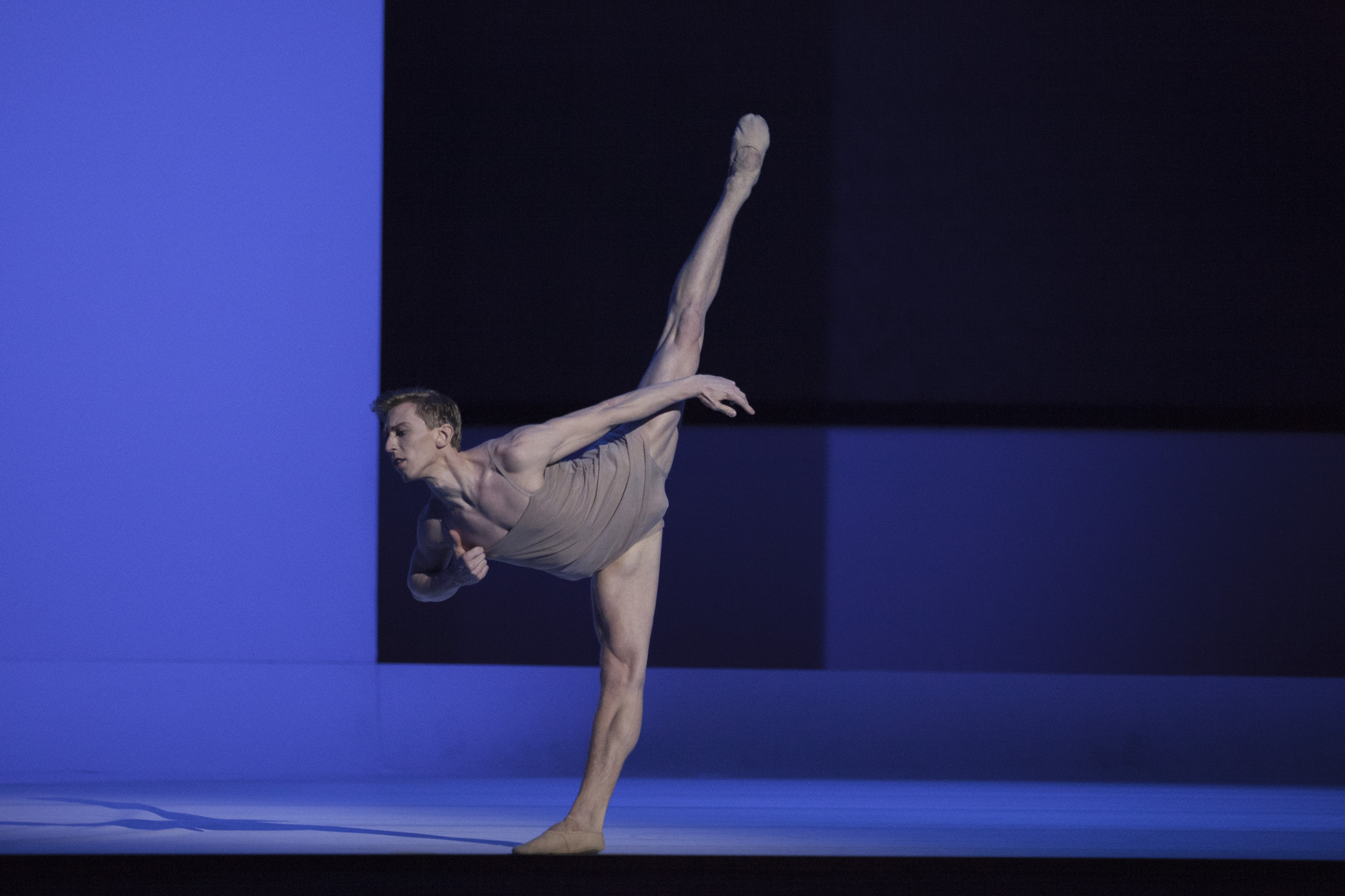 na zdjęciu tancerz z blond włosami w cielistym kostiumie, lewa noga w szpagacie uniesiona do góry, autor zdjęcia Ewa Krasucka