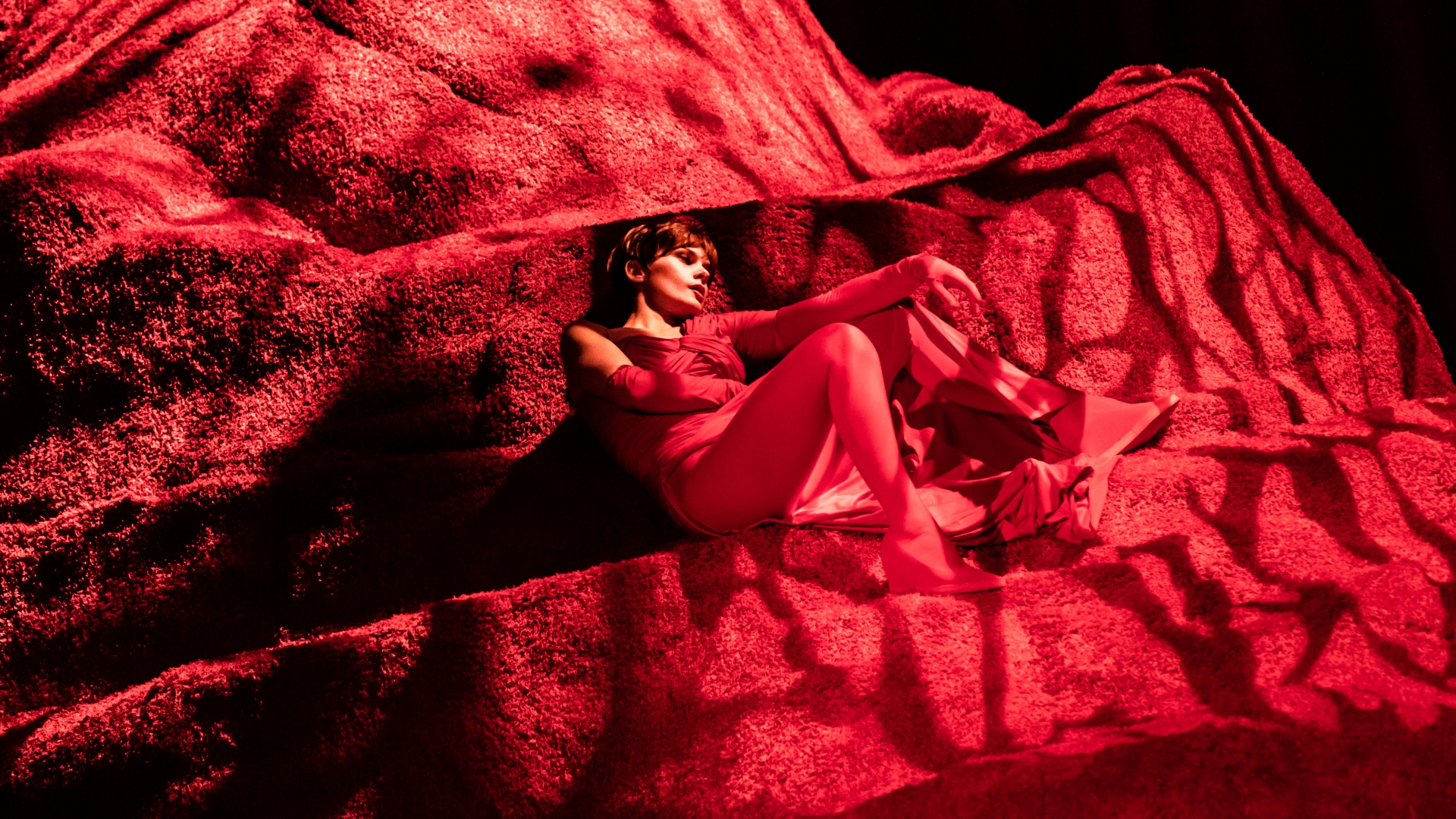 Young woman dressed in a red reclines on a red rock imitating structure